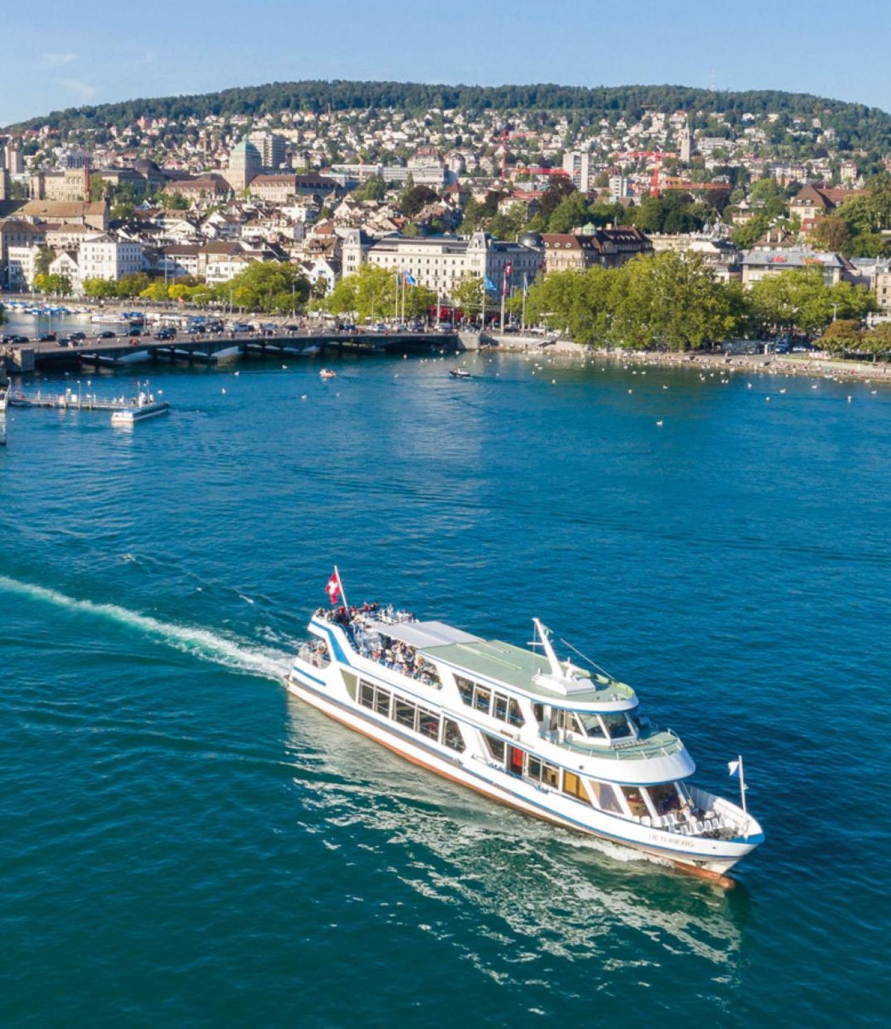 Ein Swissness Bild mit der Stadt Zürich im Hintergrund, See und einem Schiff im Vordergrund - Mobile Version